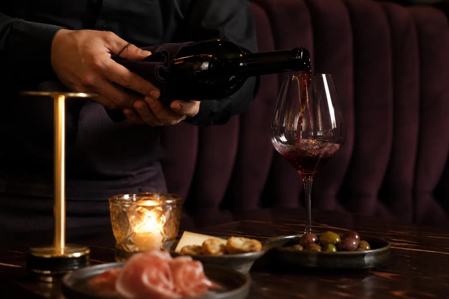 Red wine poured beside candlelit small plates